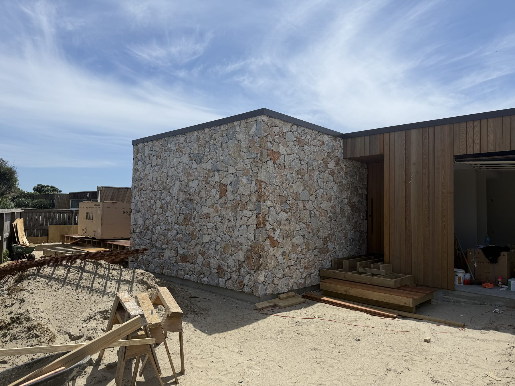 Random-laid natural stone facade beside cedar cladding on a beach build